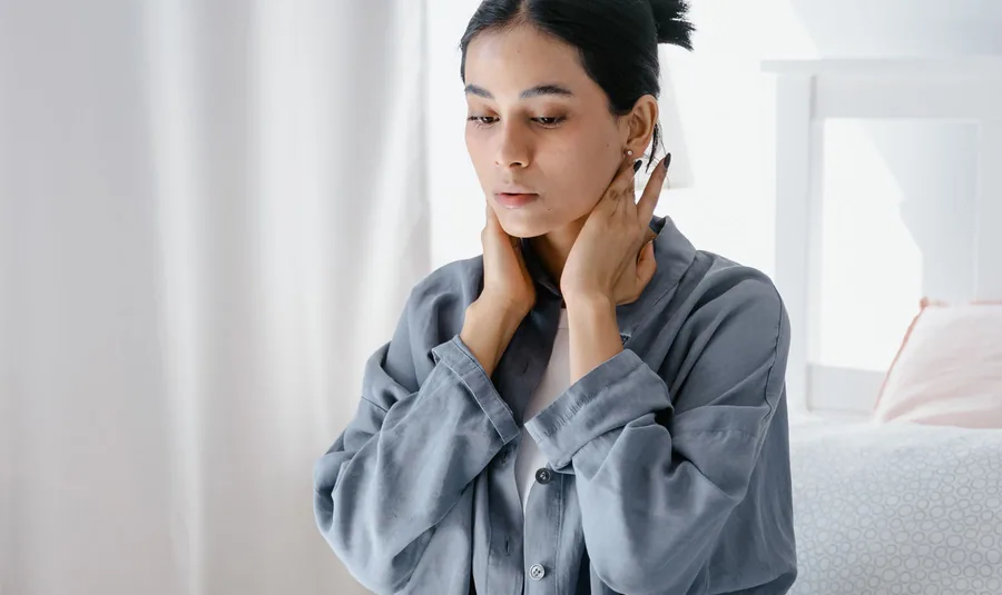 Young Asian woman at a laptop holding both sides of her neck, the typical site of office syndrome neck pain