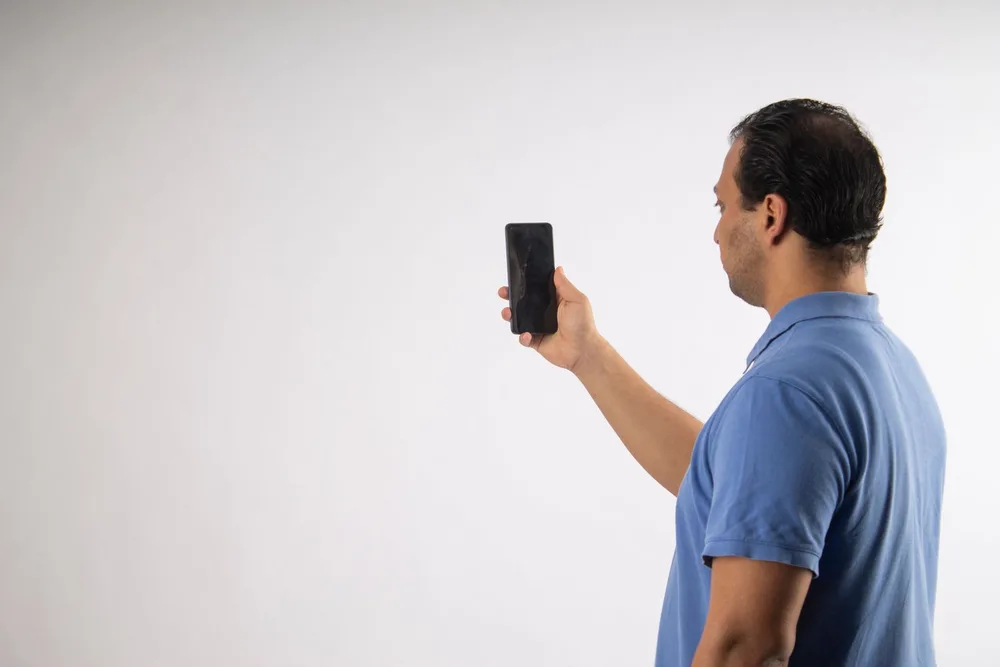 Side view of a man holding his phone up at eye level with his head level, not tipped forward