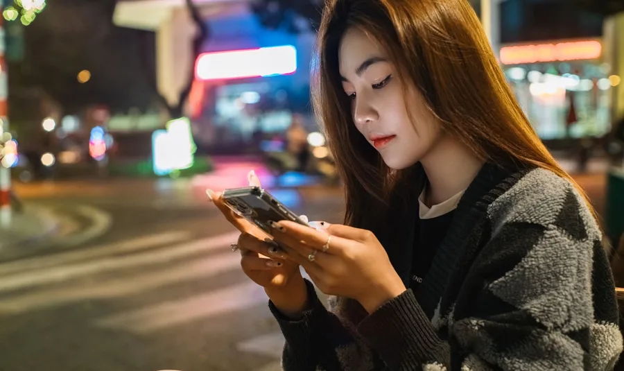 Side view of a young Asian woman looking down at her phone with her head tipped well forward, the text neck posture