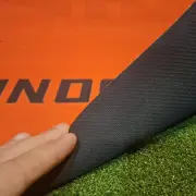 Hand on the printed orange surface of the mat next to the black textured edge, laid on turf