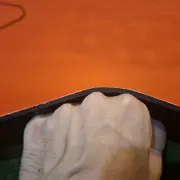 Corner of the orange mat lifted by hand to show its thickness and the black non slip underside