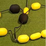 Close view of the black and yellow foam balls threaded on the rebound net cords, lying on artificial turf