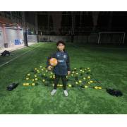 Young goalkeeper holding a ball in front of the rebound net, with a water-filled base at each front corner